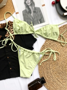 Flat lay of mint green ruched bikini set with leopard print cardigan and beach accessories