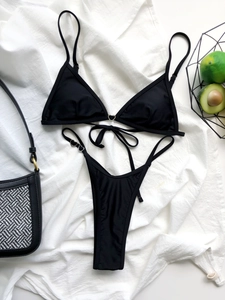 Flat lay of black triangle bikini set with heart-shaped metal rings on white fabric