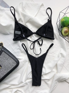 Detail of black bikini set with adjustable straps and care label on white textured fabric
