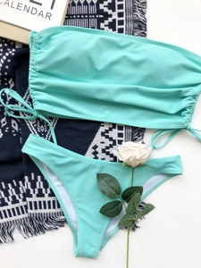 Flat lay of a mint green drawstring bikini set with a bohemian beach tapestry backdrop