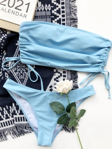 Flat lay of sky blue drawstring bandeau bikini set on a decorative textured blanket
