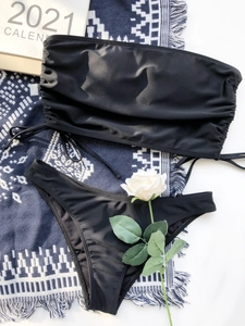 Flat lay of a sexy black drawstring bandeau bikini set with high-cut bottoms and silky fabric