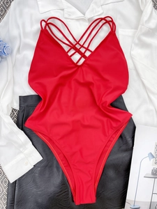 Rood badpak uit één stuk met kruisbanden op witte en zwarte kleding gelegd
