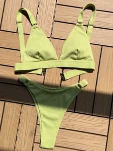 Close-up of sage green ribbed bikini set with metal ring details on a wooden deck