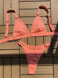 Flat lay of coral orange ribbed bikini set with metal rings on wooden background