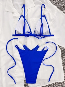 Detail of royal blue bikini with faux pearl beading and high-cut bottoms on white fabric