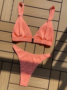 Detailed view of coral pink ribbed bikini set with metal rings on wooden deck
