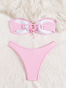 Detail of pink bandeau bikini with golden ring and adjustable ties on plush white rug