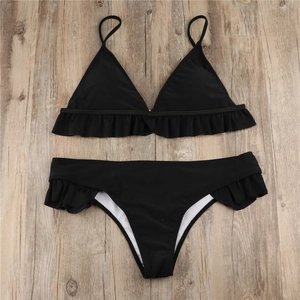 Detailed flat lay of black bikini set with lace ruffle trim on wooden background