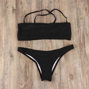 Flat lay of black two-piece bikini set with bandeau top on light wood background