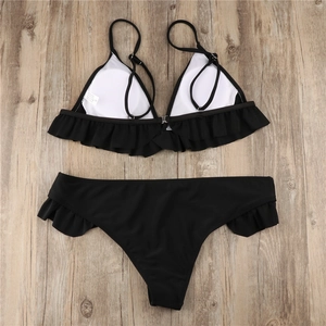 Detail of black bikini set featuring ruffled edges and textured fabric on wooden background