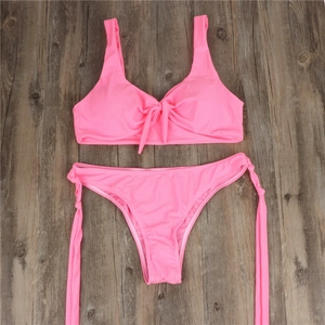 Close-up of pink bikini set with front knot top and side-tie bottoms on wood floor