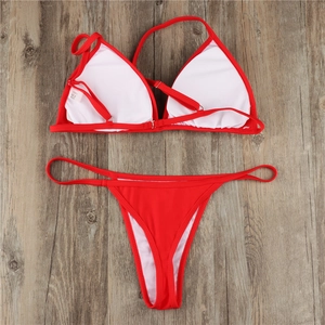 Flat lay of red triangle bikini top and high cut bottoms on dark wood texture floor