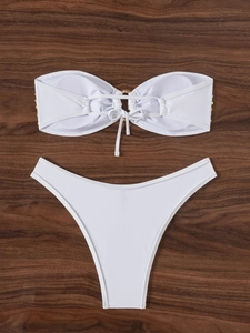 Flat lay of white bandeau bikini with golden ring detail on dark wood background