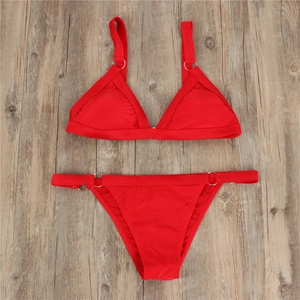 Flat lay of red bikini set featuring modern silver metal rings on a wood background