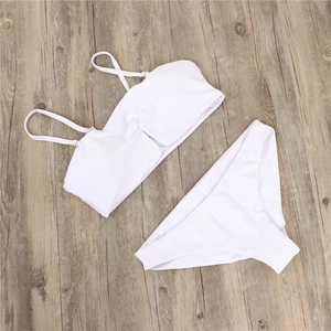 Detailed flat lay of white two-piece bandeau bikini set on a light wood floor background