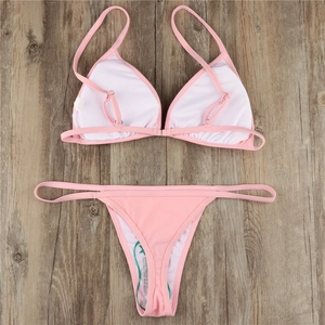 Flat lay detail of pink triangle bikini set on wood floor showing hygienic protective liner