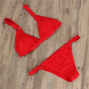 Detailed flat lay of red bikini set with silver metal rings on wooden floor