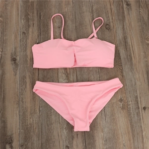 Overhead view of a light pink two-piece bikini set on a brown wooden background