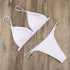 Flat lay of a white triangle bikini set with thin straps on light wood background