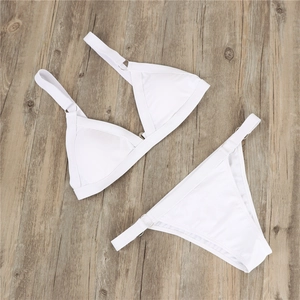 Flat lay of white bikini set with metal rings on wooden floor background