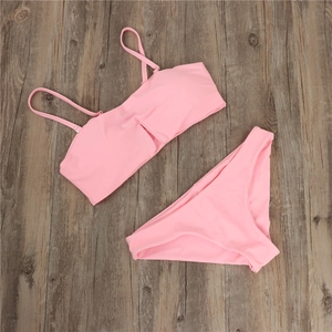 Flat lay of a pastel pink two-piece bikini with adjustable straps on a wooden floor