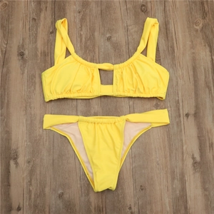 Flat lay of bright yellow two-piece bikini with cutout detail on dark wood floor