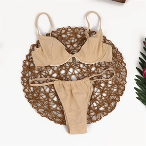 Flat lay of a two-piece nude bikini set with metal buckle detail on a woven straw mat