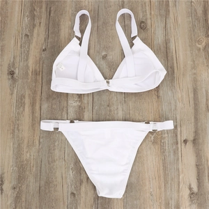 Flat lay of white bikini set with silver metal rings and size M label on wood background