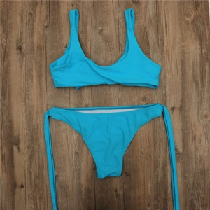 Flat lay of blue bikini set with wide straps and side-tie bottoms on wood background
