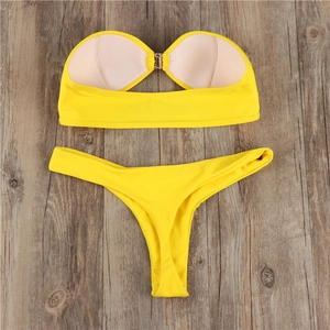 Flat lay of bright yellow bandeau bikini set with metal front clasp on wooden background