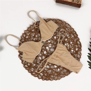 Detailed flat lay of beige bikini set with metal buckle on textured woven mat
