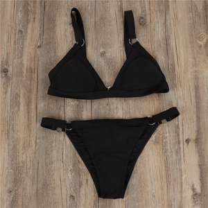Detail of black two-piece bikini with metallic ring accents on wooden background