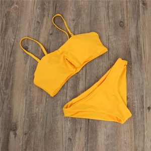 Flat lay of a bright yellow bikini set with cut-out details on dark wood background