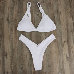 Flat lay of white two-piece bikini with triangle top and high cut bottoms on wood