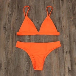 Flat lay of bright orange bikini set with triangle cups on dark wood background