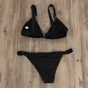 Detail of black bikini set with metal rings and white care label on wood background