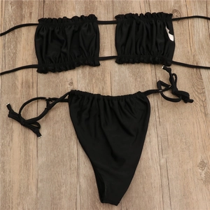 Flat lay of black ruched bandeau bikini set with side-tie bottoms on wood texture