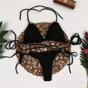 Flat lay of black halter bikini with silver rings on a decorative woven mat