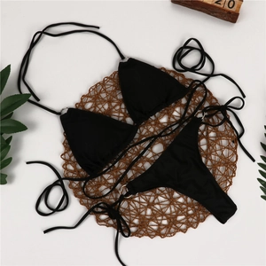 Flat lay of black bikini set with metal rings and adjustable straps on straw mat