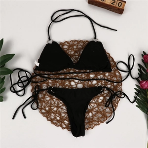 Flat lay of a black string bikini set with metal rings and floral decor on a woven mat
