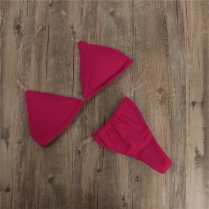 Flat lay of rose red three-piece bikini with transparent straps on wooden floor