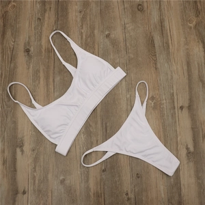 Flat lay of white two-piece bikini set with thin straps and elastic band on wooden floor