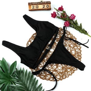 Flat lay of black bikini set with heart metal ring and side ties on a woven mat