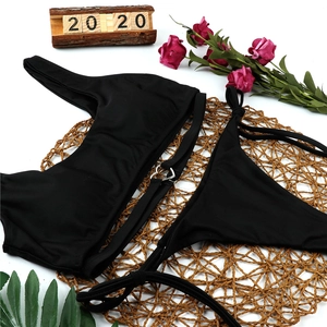 Detail of black one-shoulder bikini set featuring metal heart rings on woven mat