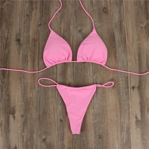 Flat lay of pink two-piece string bikini on rustic dark brown wooden background