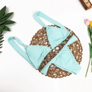 Flat lay of light mint green two-piece bikini set with pleated cups and side ties on woven mat