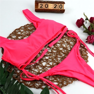 Detail of hot pink bikini set with a metal heart buckle on a woven summer resort background