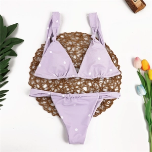 Detailed flat lay of lavender polka dot bikini set on a woven mat with floral accents