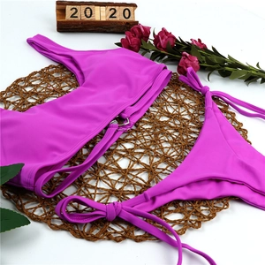 Flat lay of purple one shoulder bikini with metal ring detail on woven mat with roses